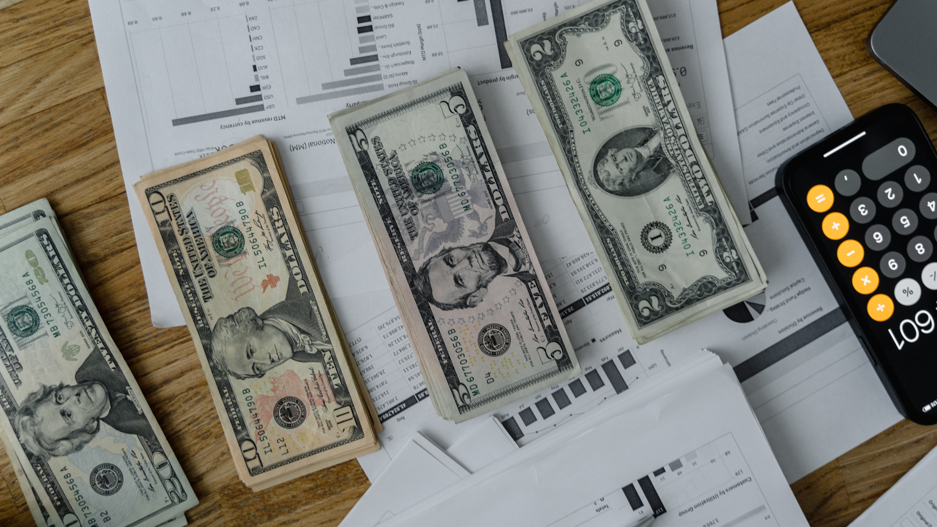 A bunch of money is sitting on top of a table next to a calculator.