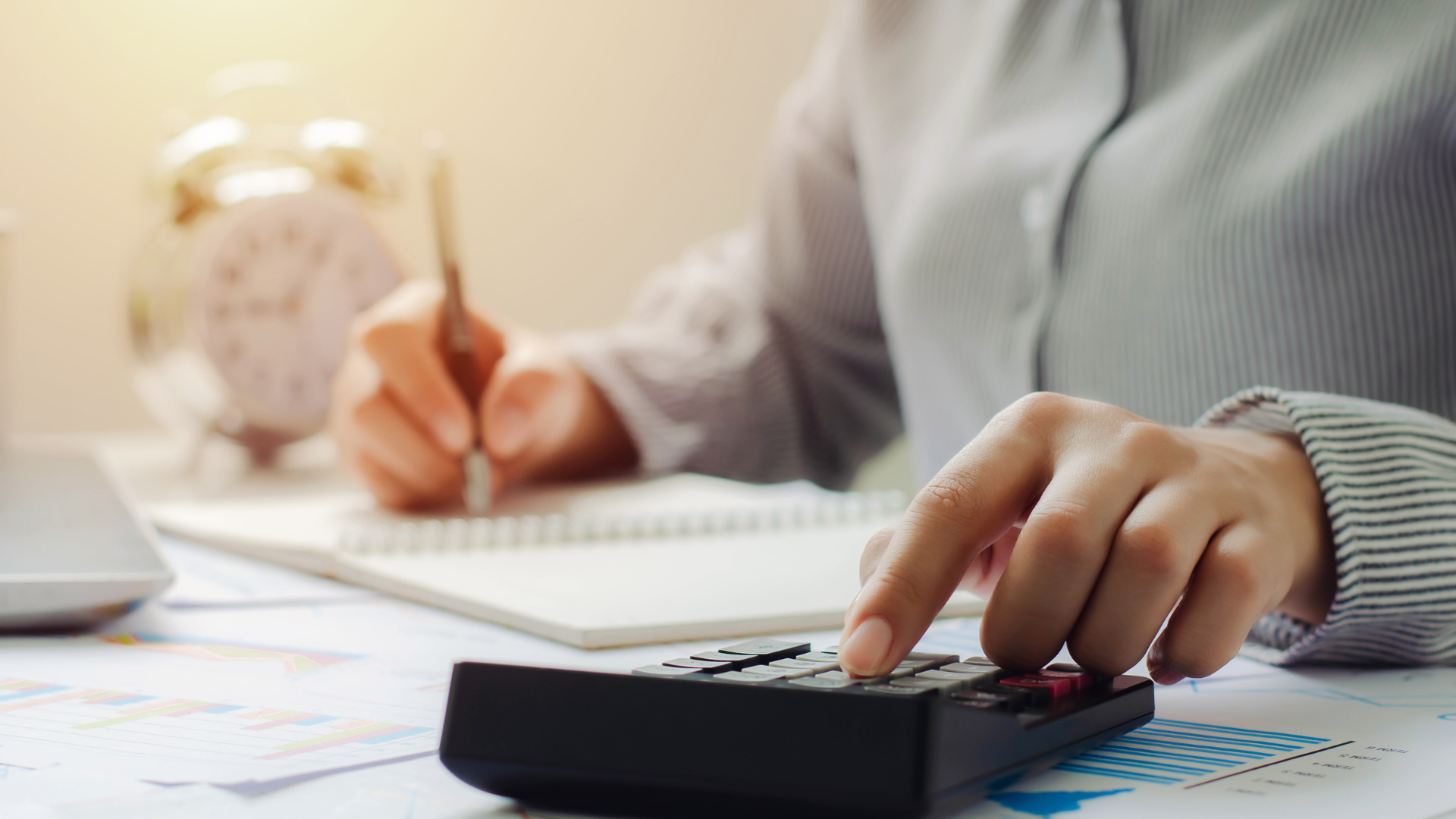 A woman is using a calculator while writing in a notebook.