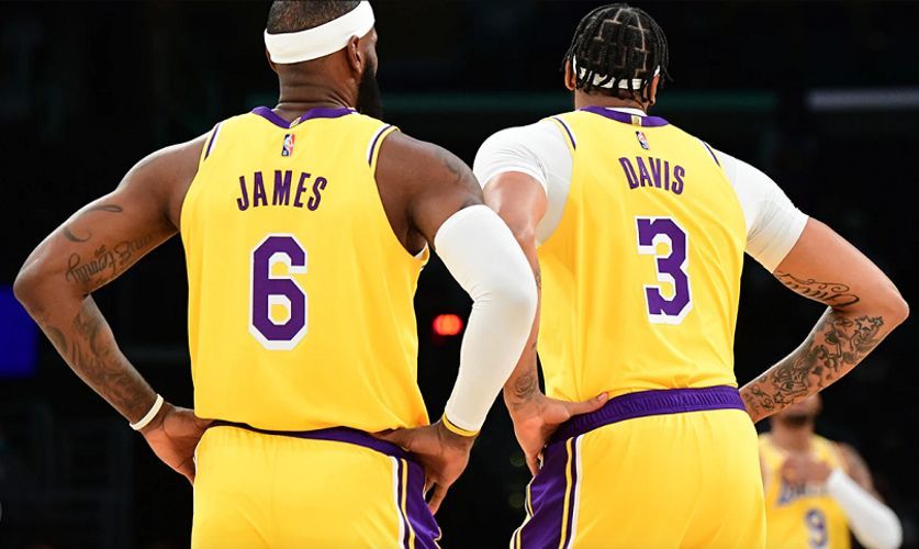 a couple of LA Lakers basketball players standing next to each other with their hands on their hips.