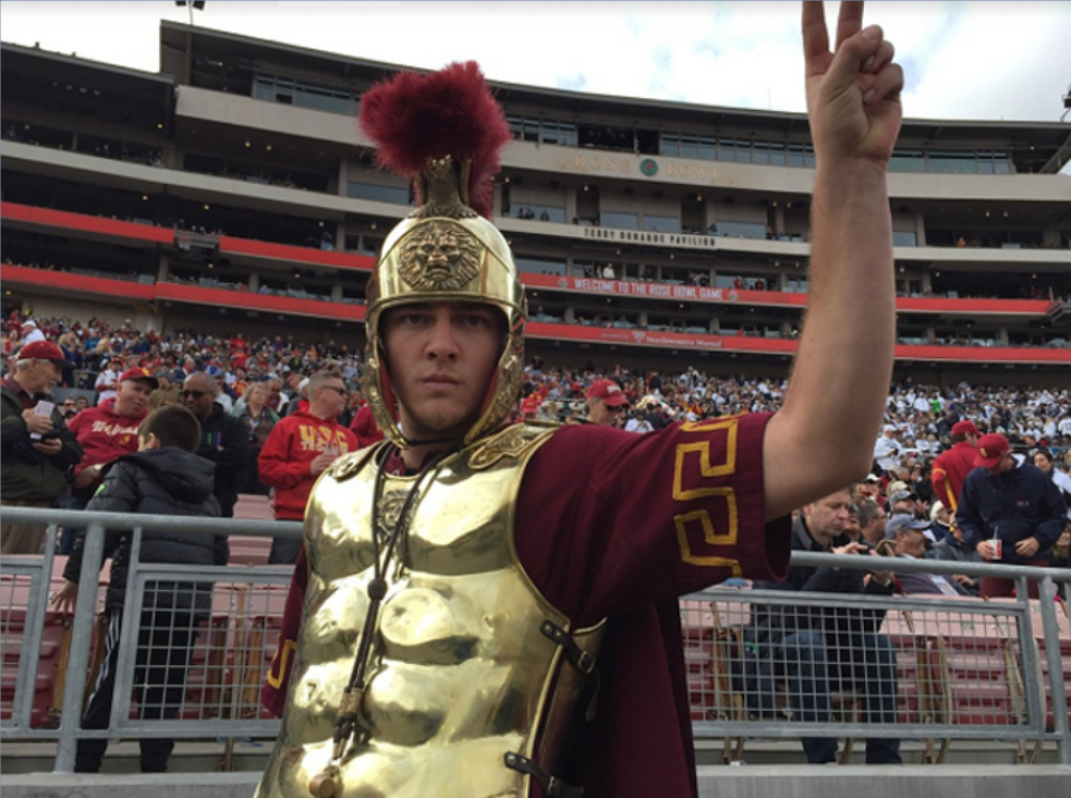 a man rooting for the USC Trojans dressed as a roman soldier is giving a peace sign .