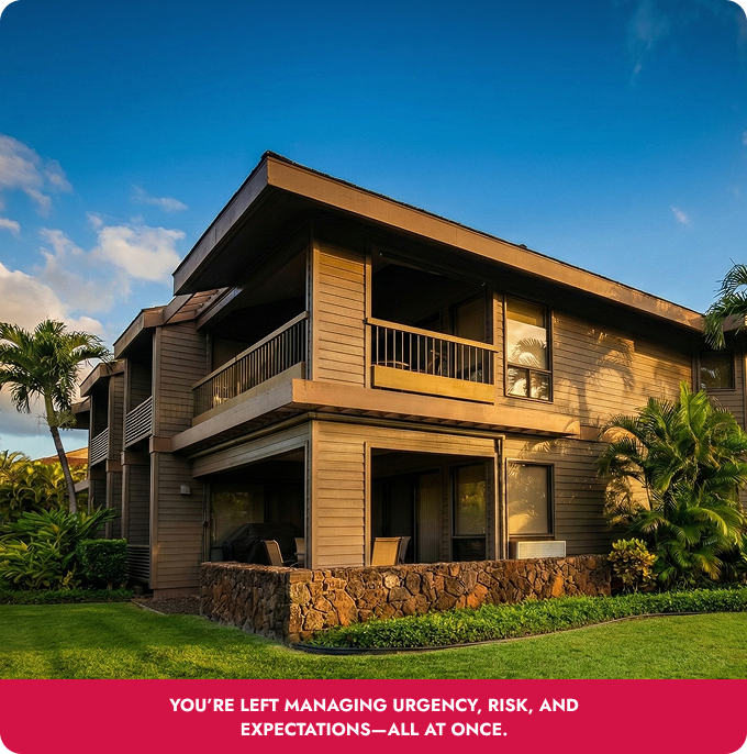 Modern two-story wooden house with balcony, stone base, and lush tropical landscaping under a blue sky