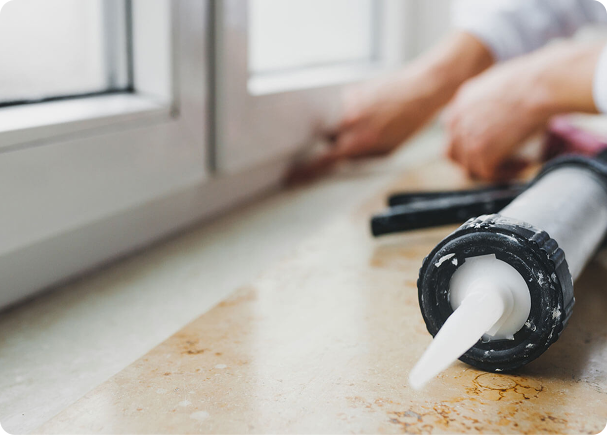 Caulking gun applying sealant along a windowsill beside a white window frame