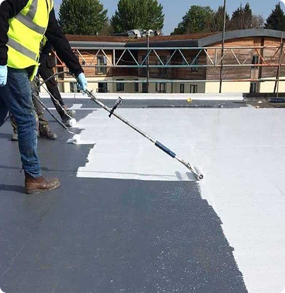 Worker applying white coating to a flat rooftop with a roller, leaving a sharp edge over dark roof membrane.