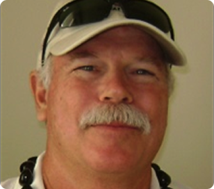Close-up of a smiling man wearing a tan cap and sunglasses, with a mustache