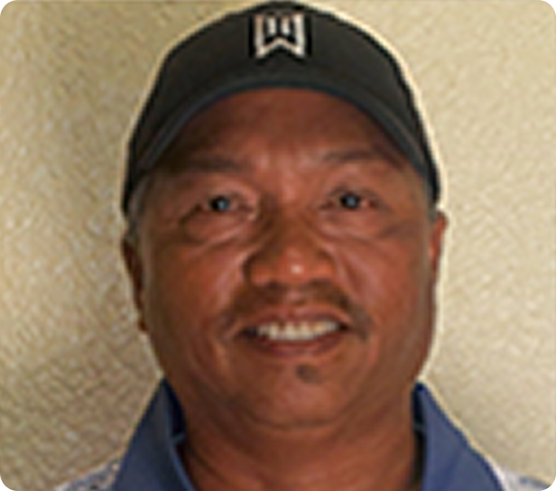 Smiling man in a black cap and blue shirt against a beige wall
