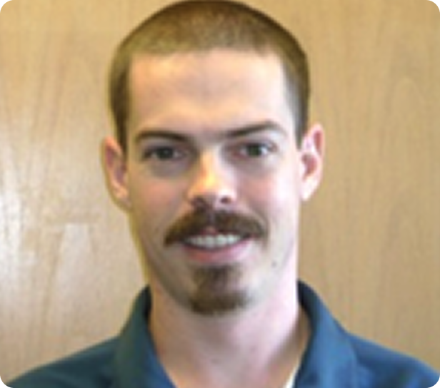 Man with short hair and goatee, smiling in front of a wooden background