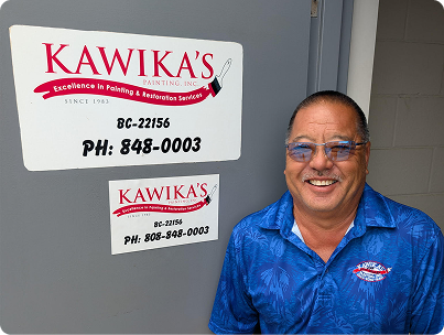 Man smiling beside Kawika's signage on a gray wall.
