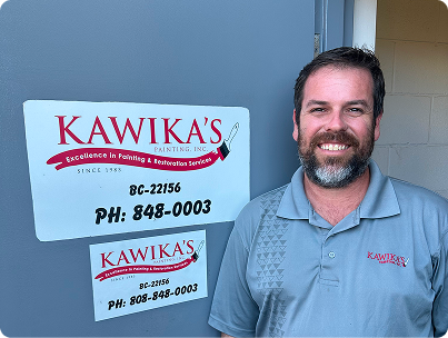 Man standing beside a Kawika’s sign, smiling in a gray logo shirt.