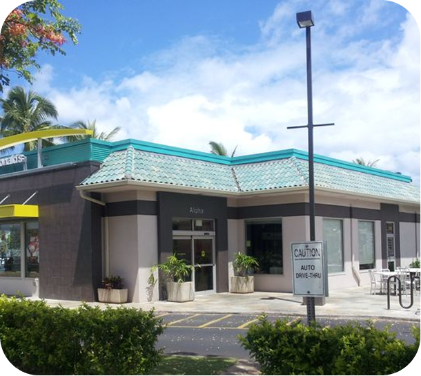 Modern low-rise storefront with teal trim, cloudy sky, and a parking sign in front
