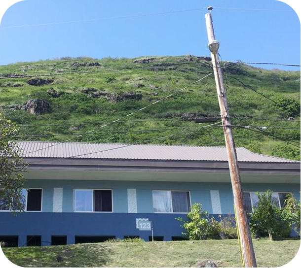 Blue building at the base of a green hillside, with a utility pole in the foreground.