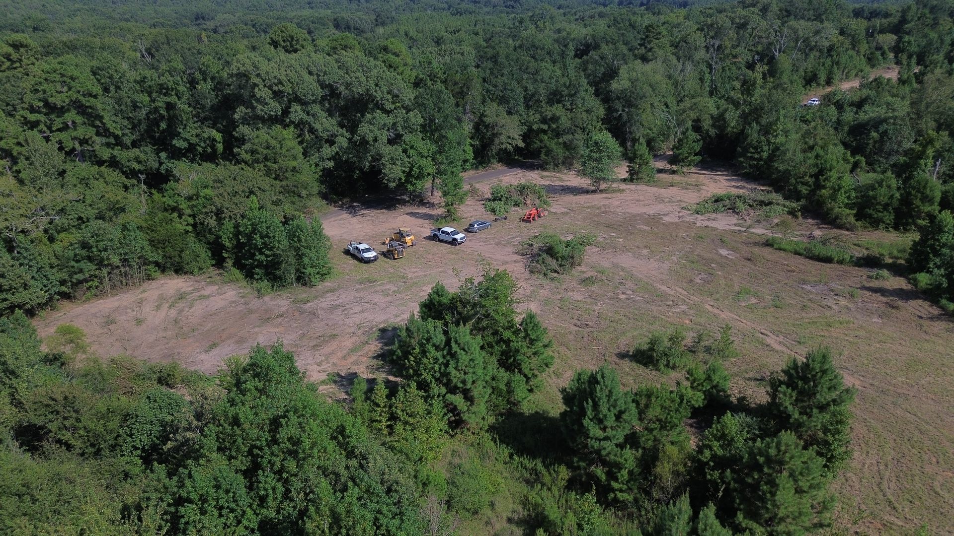 Aerial view of a deforested area in a forest with vehicles and people present.
