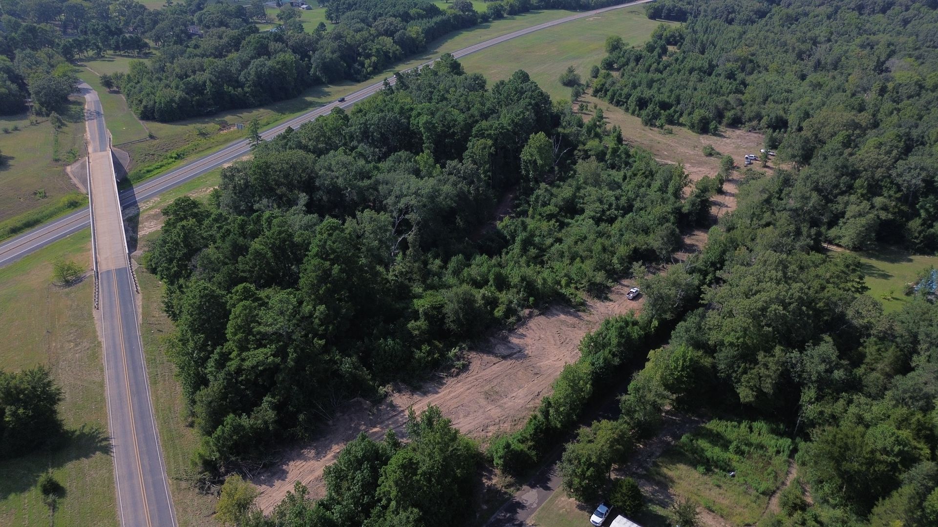Aerial view of a wooded area next to a road and bridge, with green trees and brown earth.