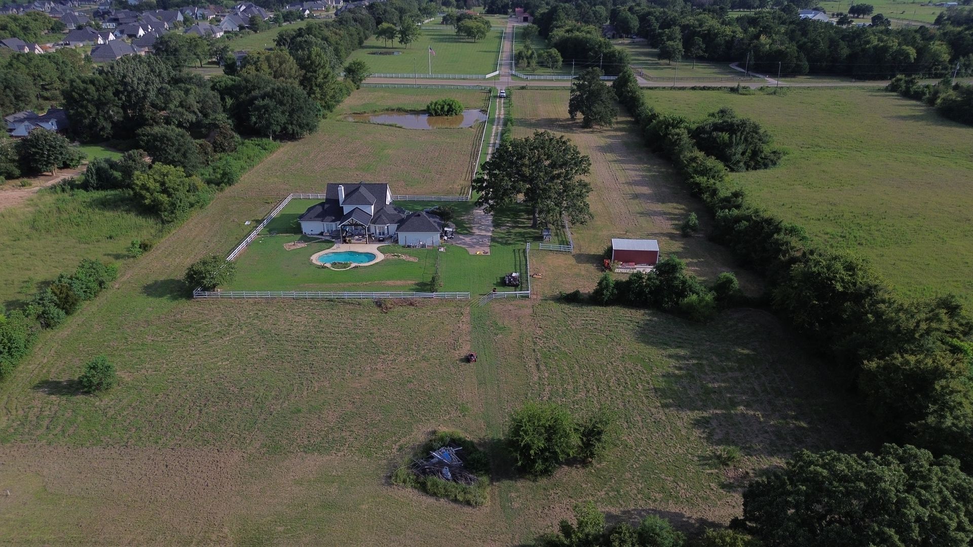 Aerial view of a large house with a pool and red barn on expansive green property.