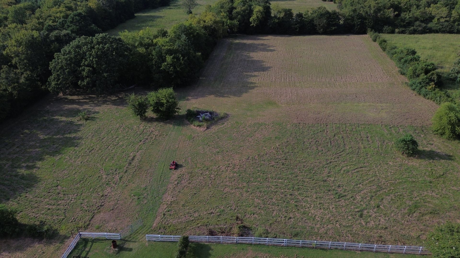 Aerial view of a field with a few trees, grass, and a small building.