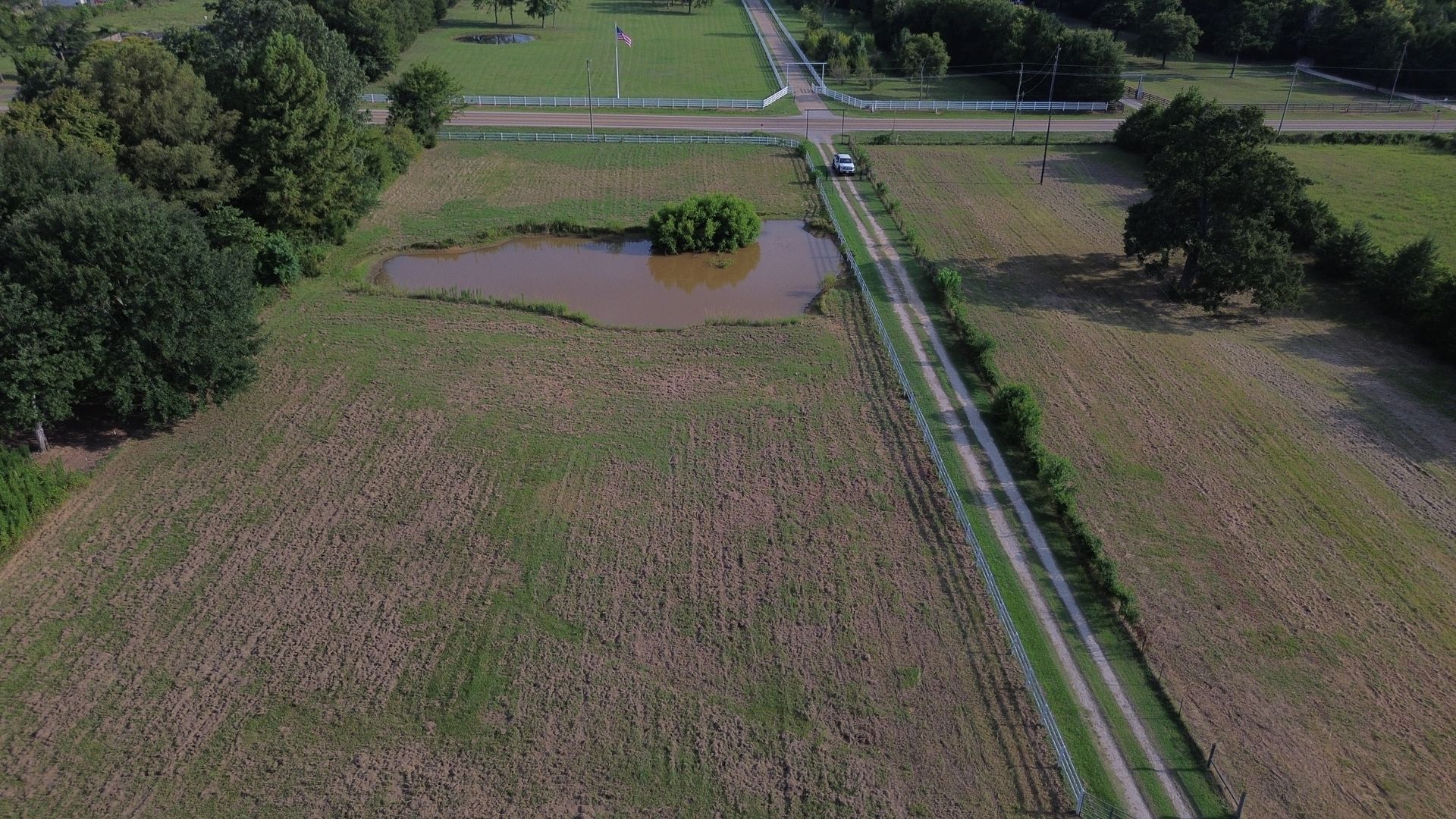 Dirt road through a field with a pond and a vehicle near a crossroad.