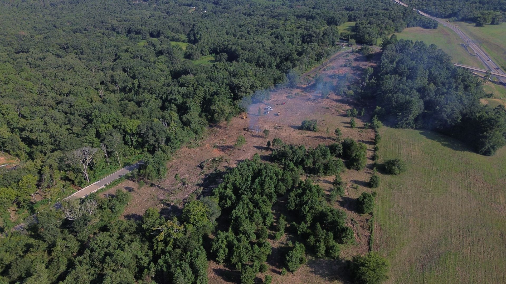 Aerial view of a plane crash site in a clearing, with smoke rising and debris scattered amid trees.