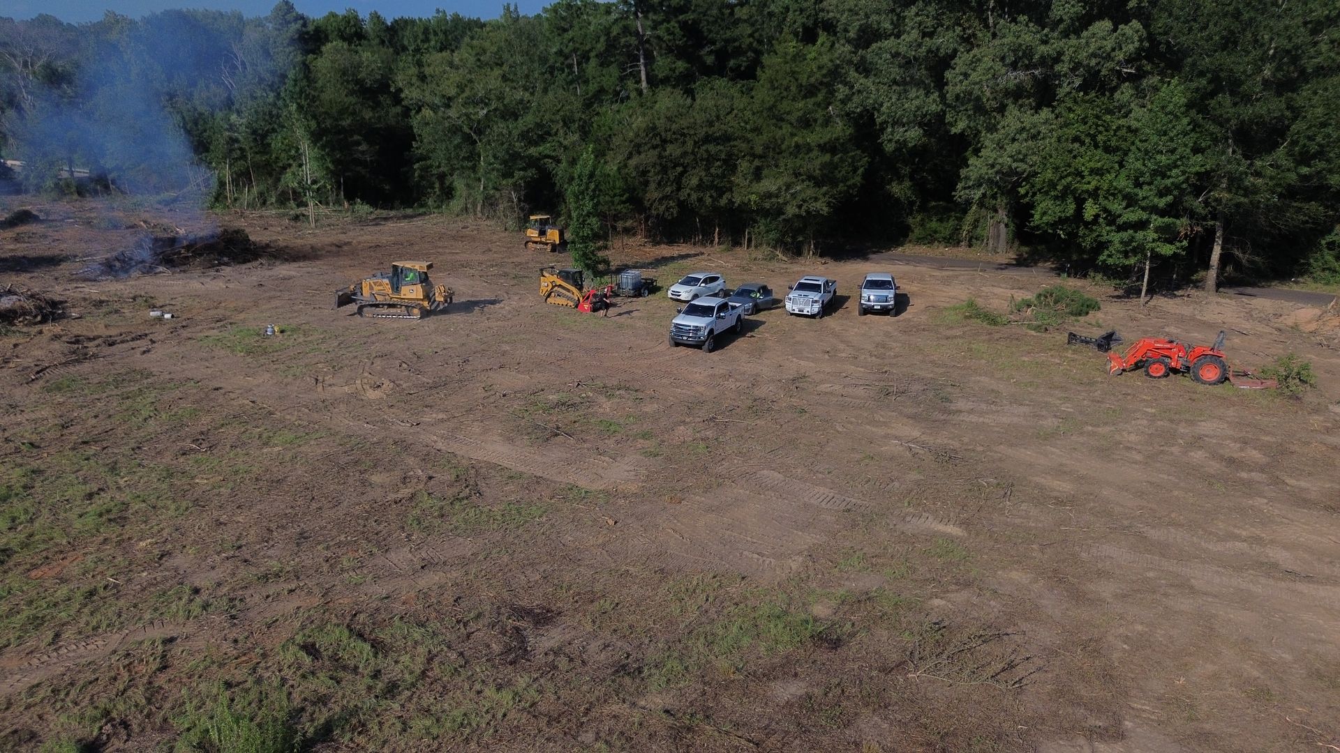 Clearing of a forest: bulldozer, vehicles, and machinery on a large, bare field next to remaining trees.