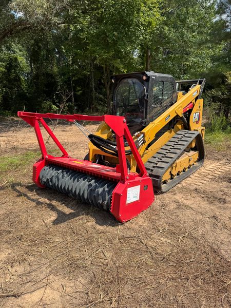 Yellow skid steer with a red brush cutter attachment on a brown field.