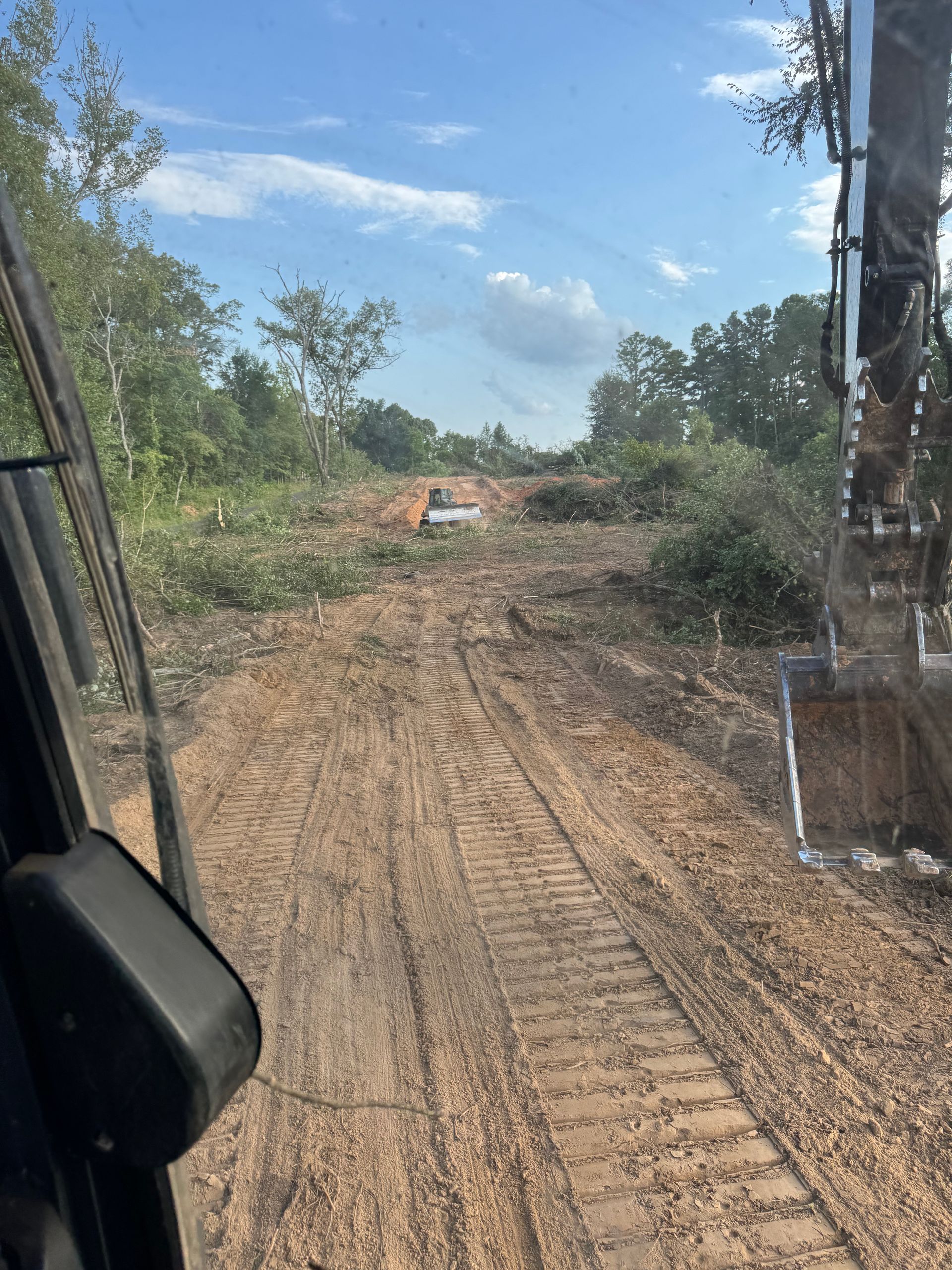 Dirt road cleared by heavy machinery, leading to a bright sky, excavator arm in view.