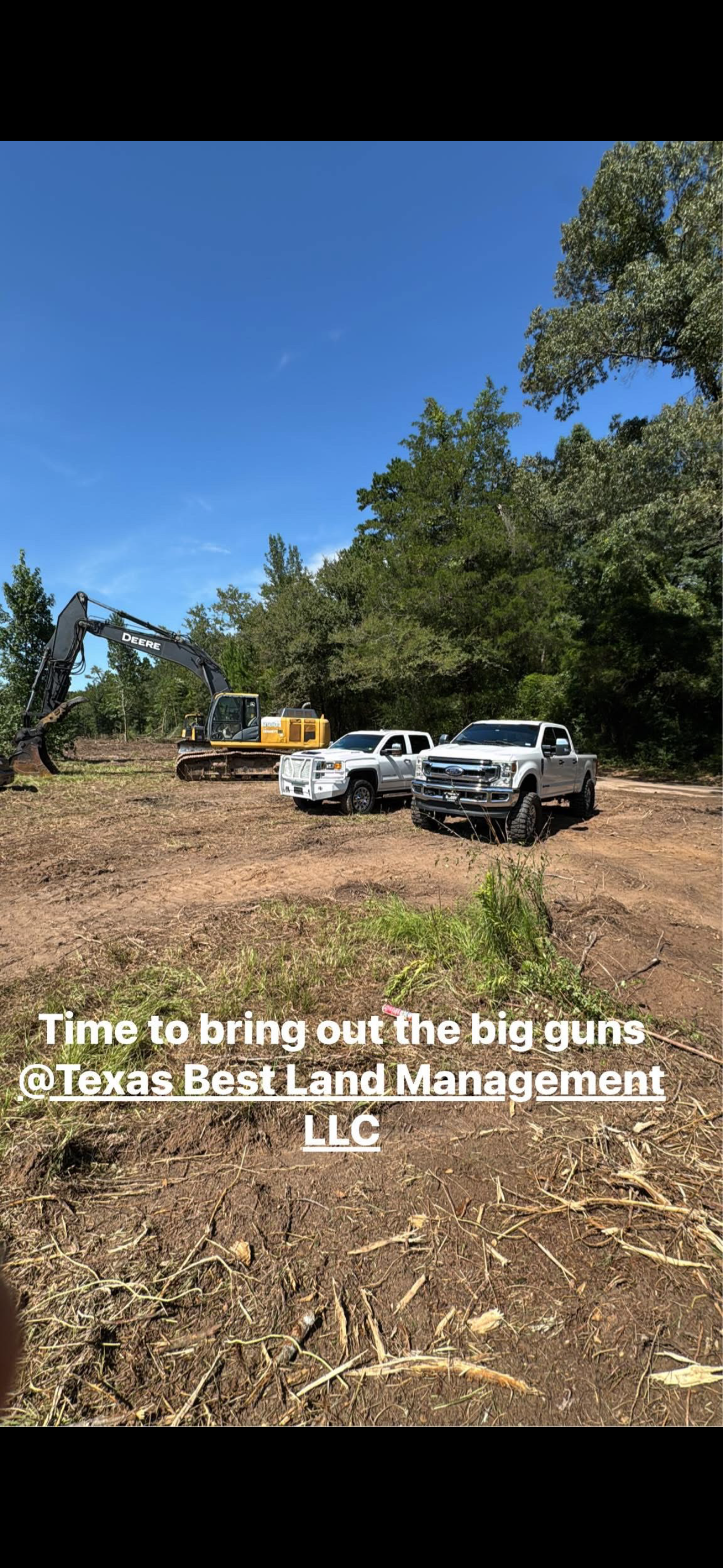 Construction site with trucks, excavator, and trees under a blue sky.