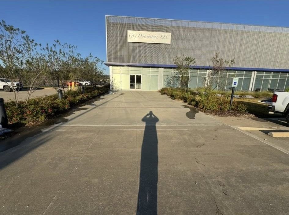 A person's shadow on concrete leading to a building with a sign that reads 