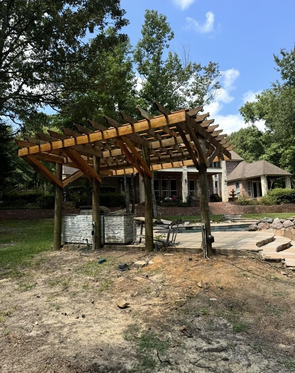 Wooden pergola in a yard, with a house in the background on a sunny day.
