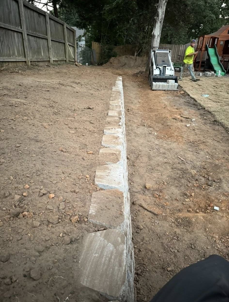 A low retaining wall built in a backyard, with a construction worker and equipment in the background.