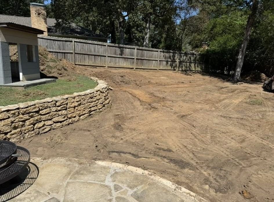 Backyard with retaining wall, dirt, wooden fence, and small building.