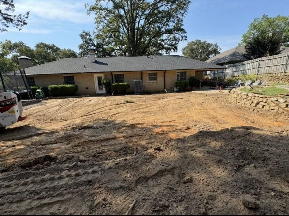 Backyard landscaping in progress, with house, dirt, and small bulldozer.