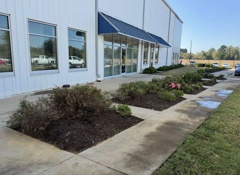 Exterior of a white building with blue awning and windows, with landscaped flowerbeds and sidewalk.