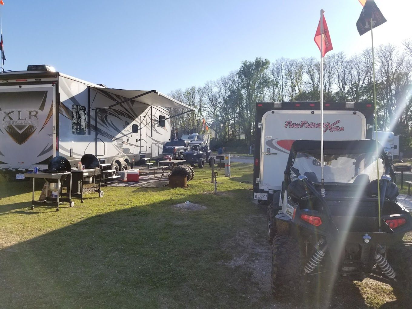 A rv is parked in a grassy area next to a trailer.