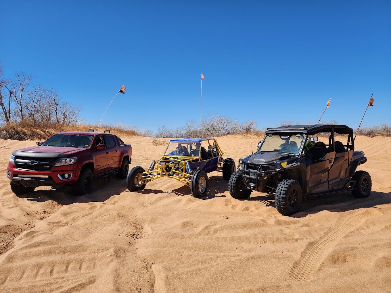 Three off road vehicles are parked on top of a sand dune.