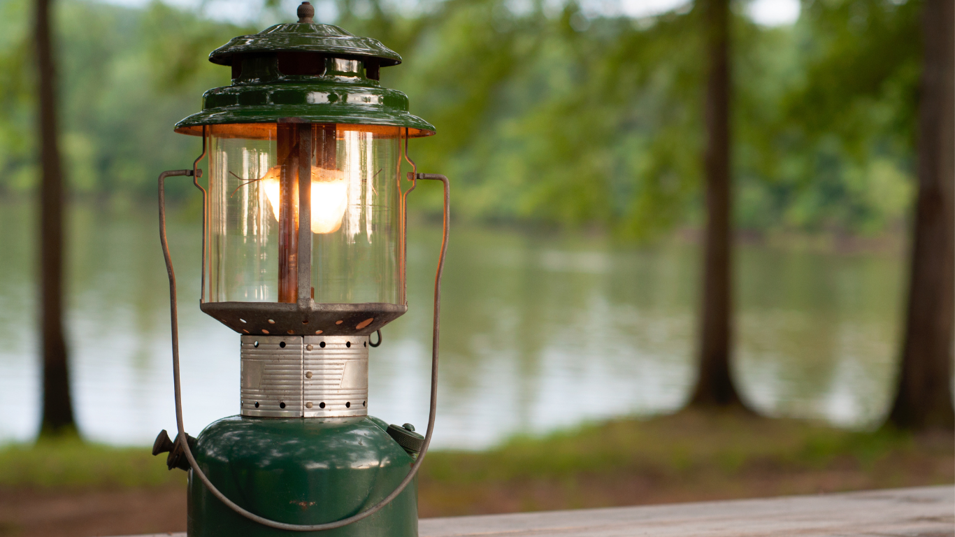 A green lantern is sitting on a picnic table next to a lake.