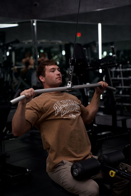 A man in a brown shirt is lifting a barbell in a gym