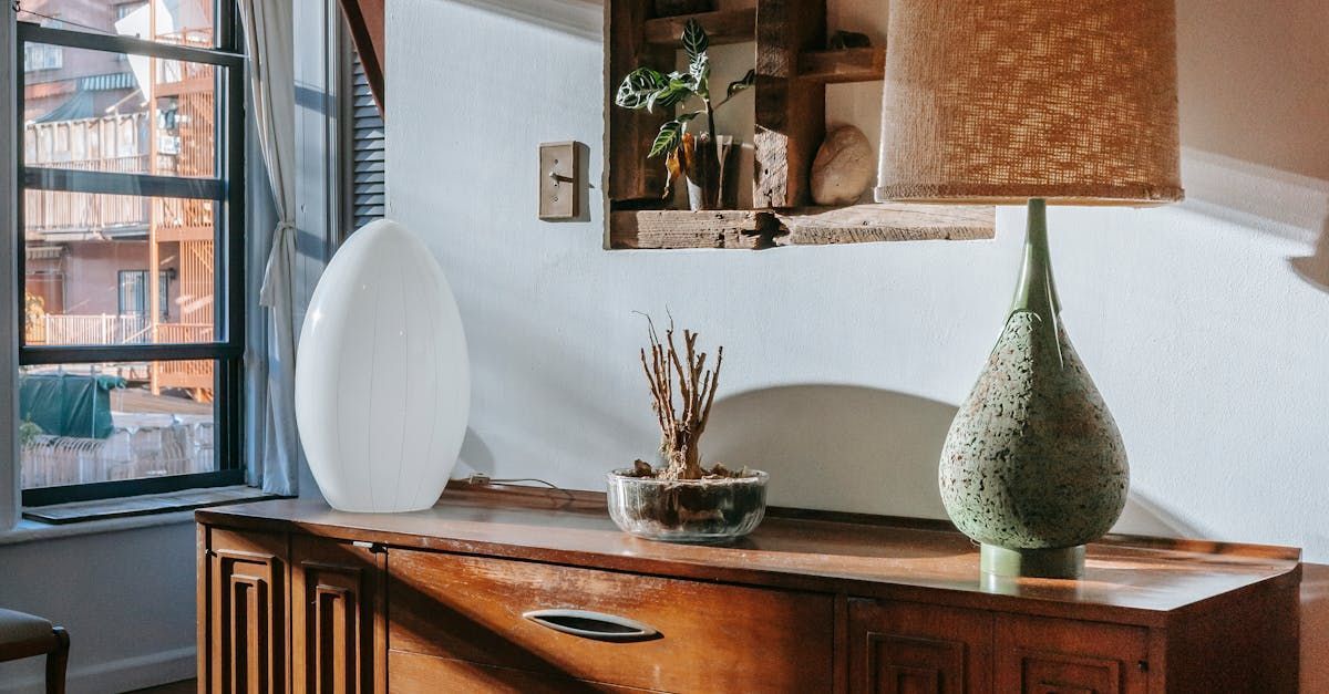 A lamp is sitting on top of a wooden dresser next to a window.