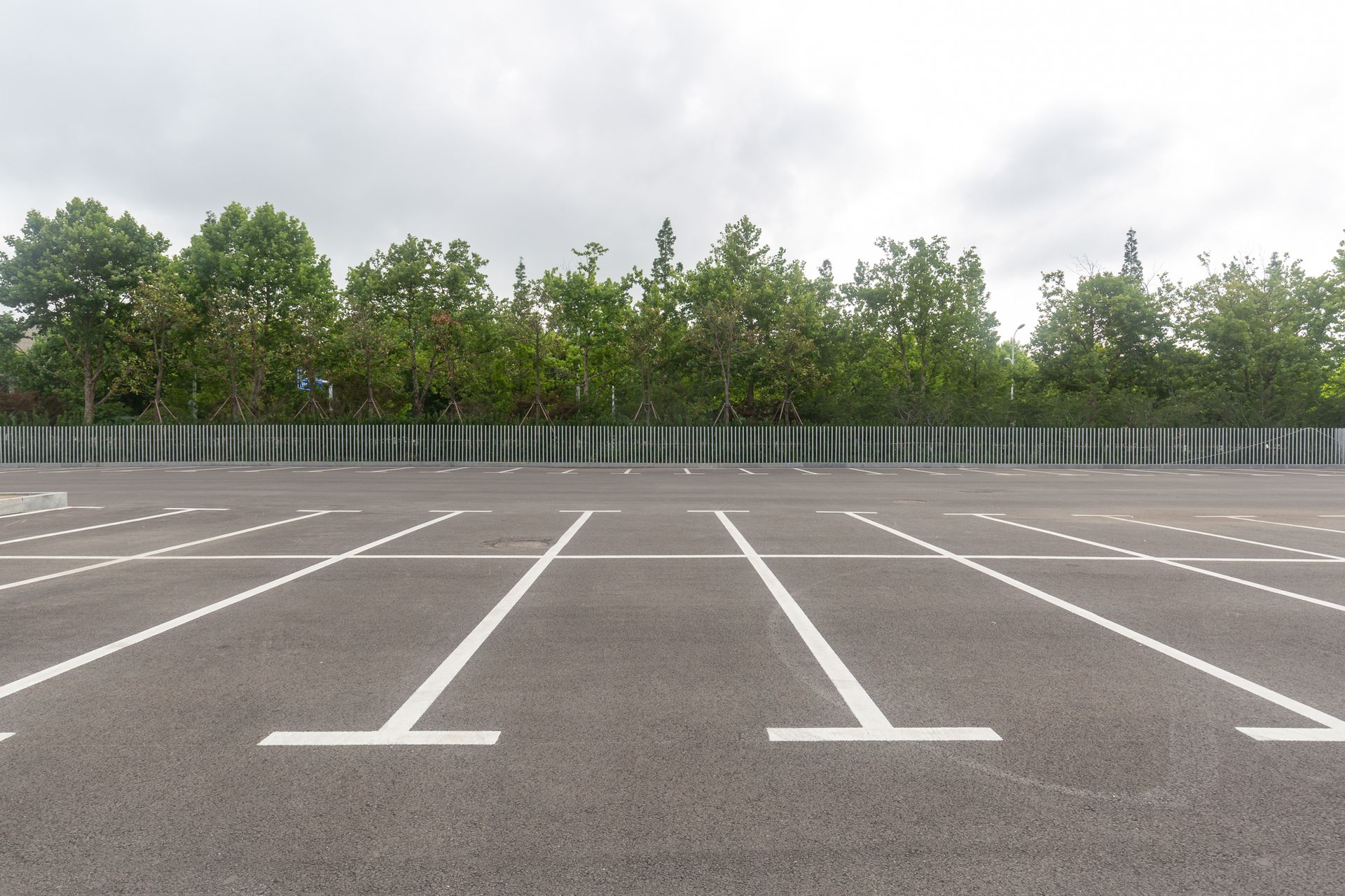 An empty parking lot with a fence and trees in the background.
