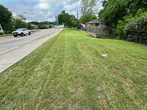 A car is driving down a road next to a lush green field.