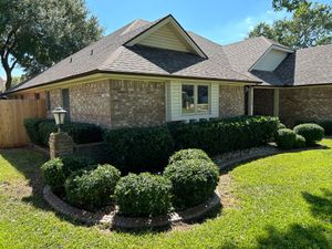 A brick house with a lush green lawn and bushes in front of it.