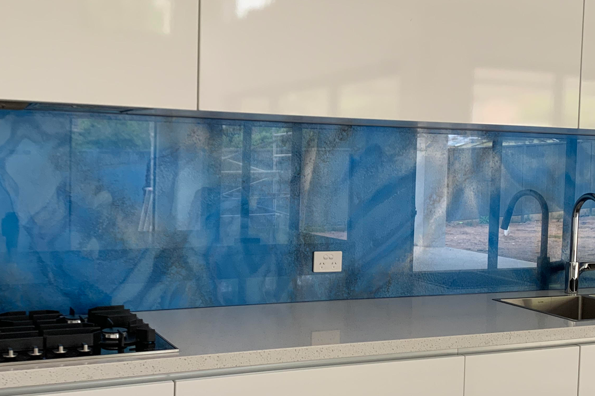 A kitchen with a blue glass backsplash and white cabinets.