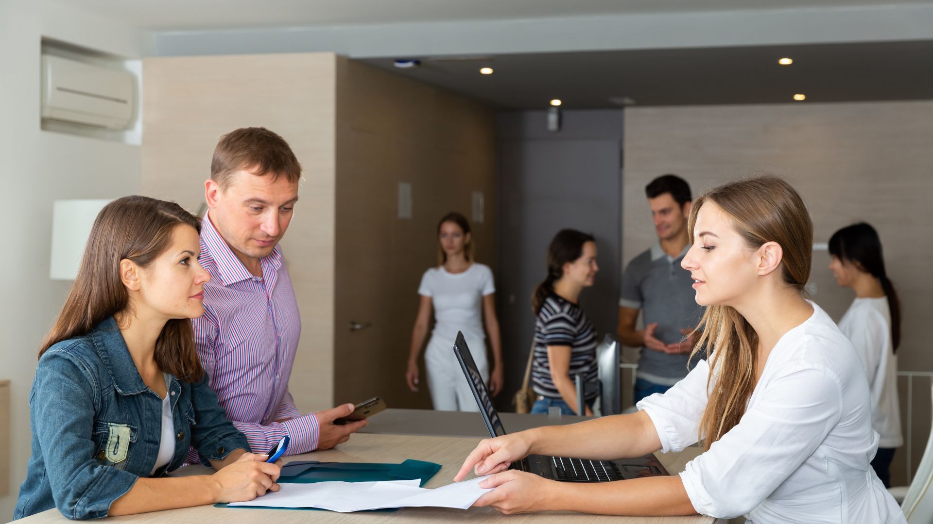 People at a table review documents, others in background, in a modern office.