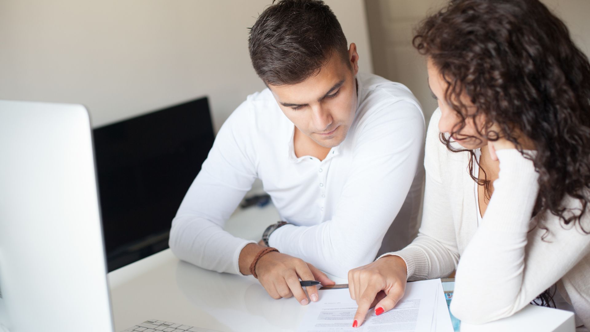 Man and woman review paperwork together at a desk. The woman points to document; the man looks on.