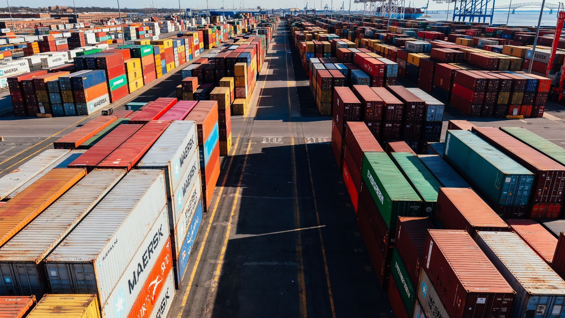 Rows of colorful shipping containers at a port, under a sunny sky.
