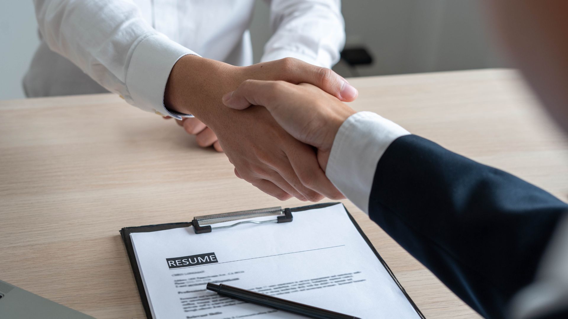 Handshake over a resume on a desk. Two people in formal attire.