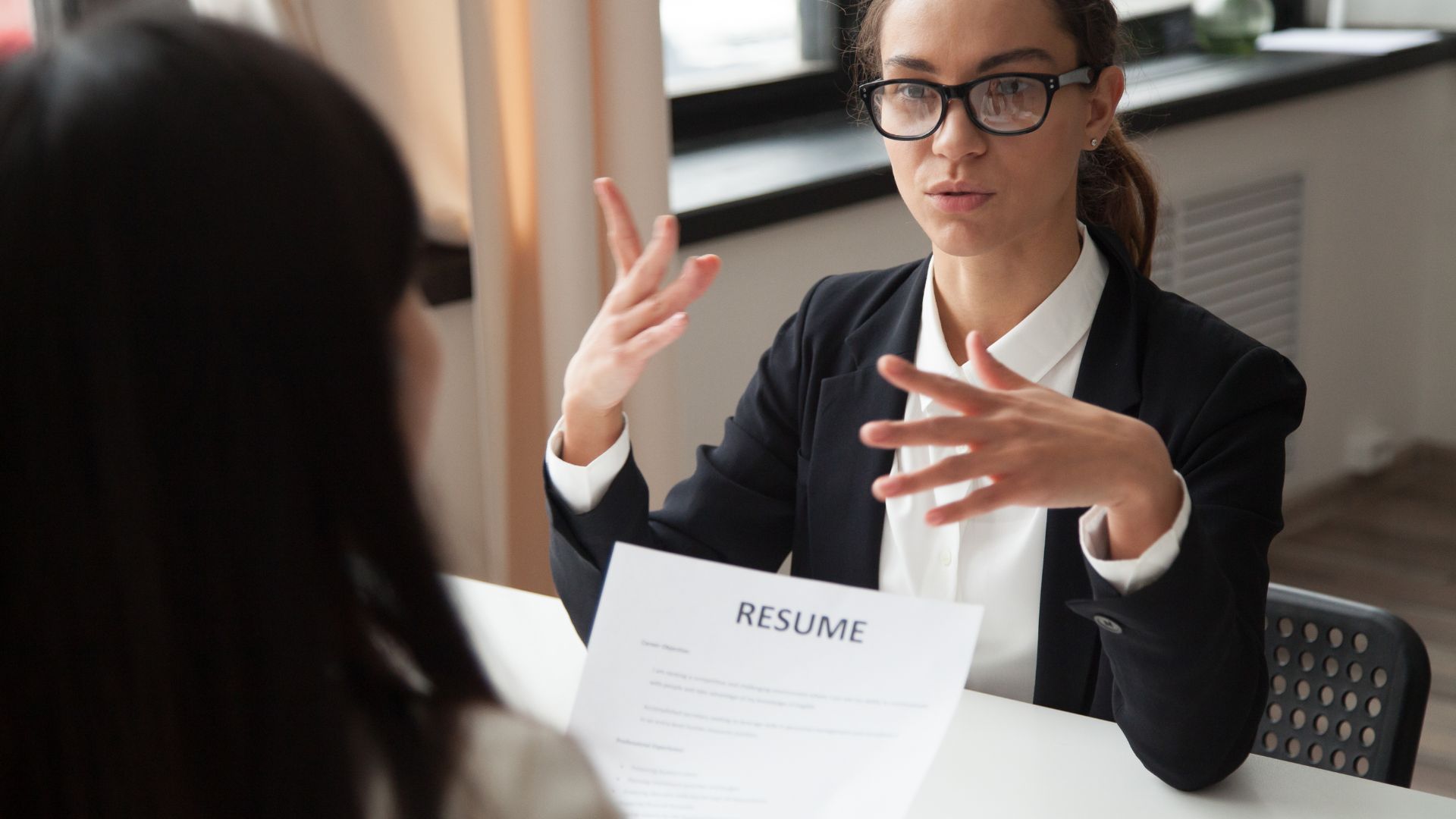 Woman in glasses gestures while reviewing a resume during a job interview.
