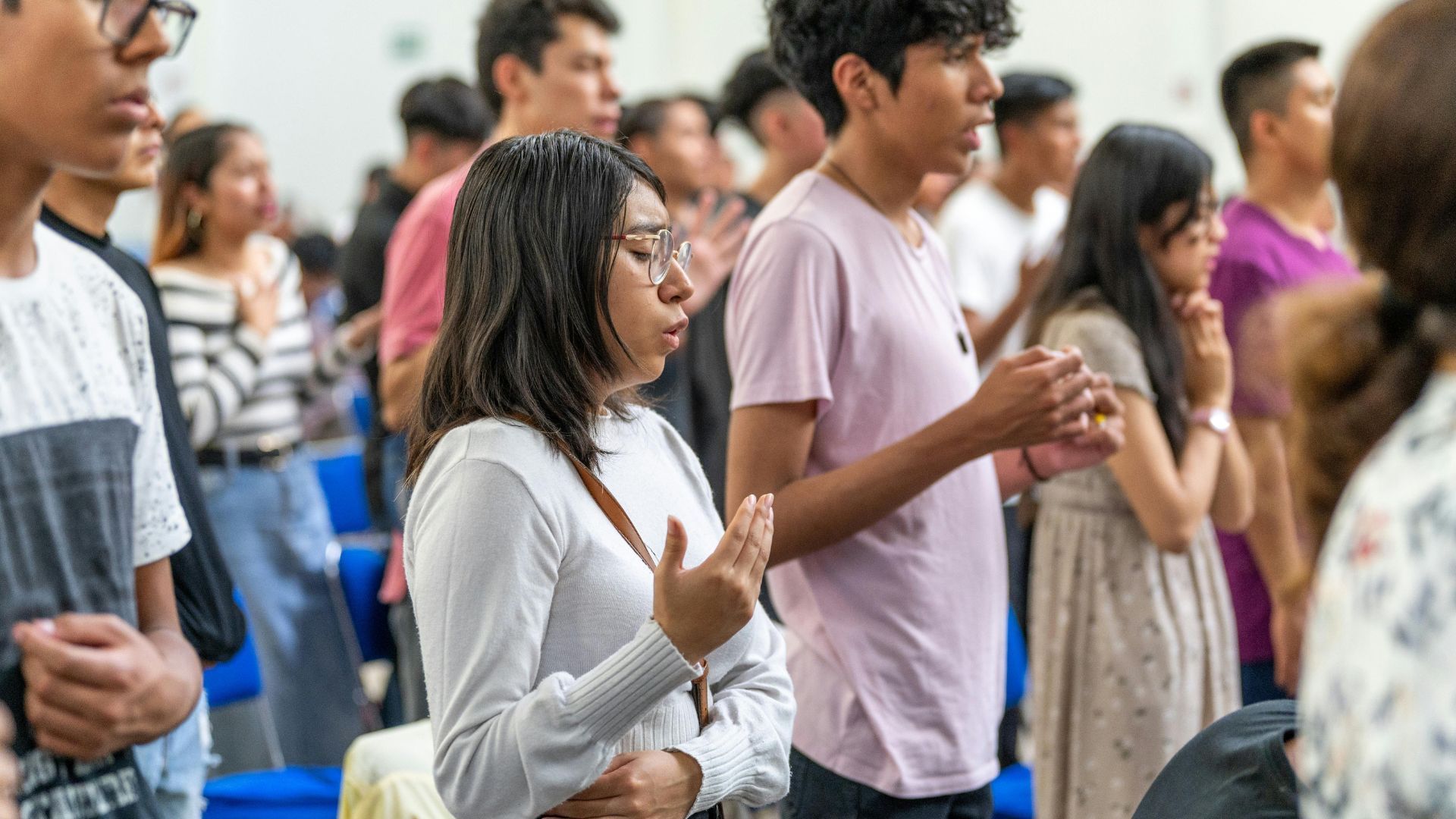 People standing together with hands raised, possibly in prayer or worship, indoors.
