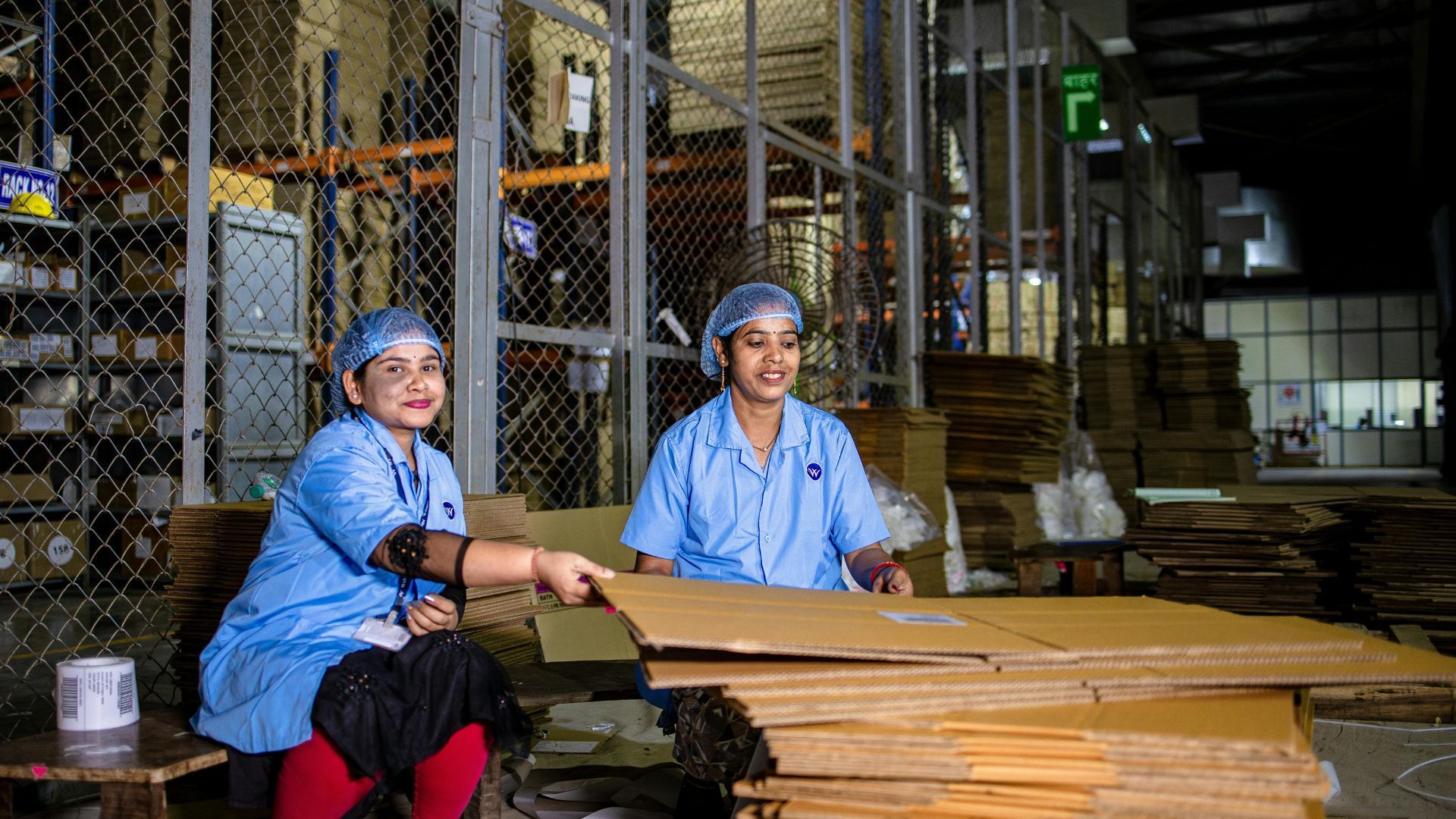 Two people in blue work uniforms sort cardboard in a warehouse setting.