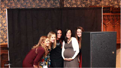 A group of women are posing for a picture in front of a black curtain.