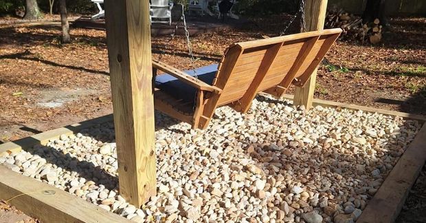 A wooden swing is sitting on top of a pile of gravel.