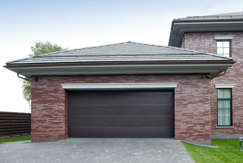 Didelis mūrinis namas su rudais garažo vartais