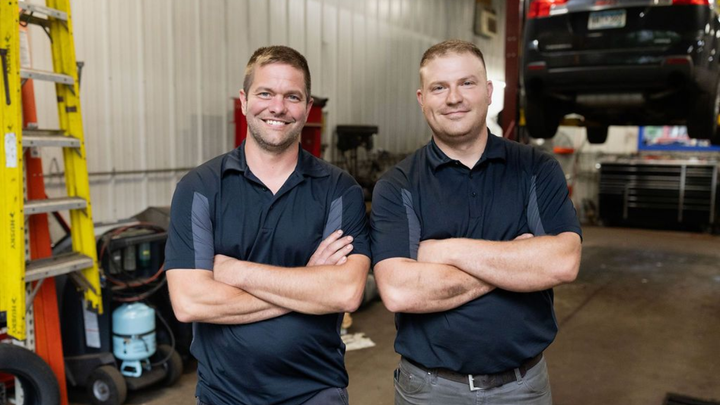 Two men in navy polos stand with arms crossed in a workshop garage.